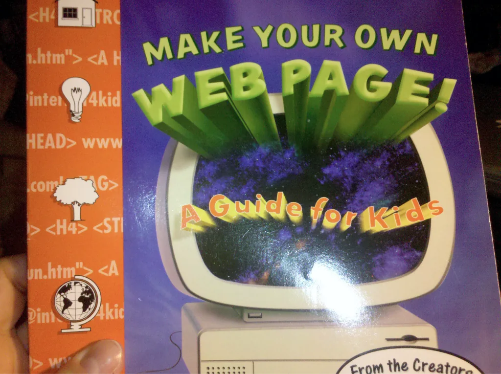 A paperback copy of “Make Your Own Web Page! A Guide for Kids”: the cover shows a glowing old computer with HTML tags around its edges.